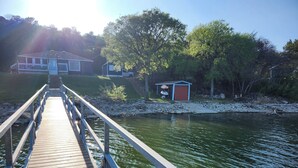 A wooden pier leading to a house with a red door, surrounded by trees and a small shed. - Wet Feet Retreat! Lake front cabin in quiet cove. (Caddo)
