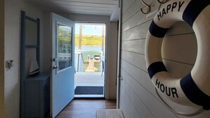 Un pasillo con piso de madera, una puerta azul y una vista hacia un área exterior con cielo despejado.