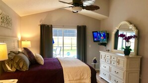 Ein Schlafzimmer mit Bett, Kommode, Fernseher und einem fenster mit Vorhängen.