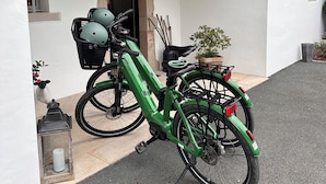 Un vélo électrique vert est garé devant un bâtiment dont l’entrée est surmontée d’une arche en pierre. On y voit également une petite plante en pot et une lanterne posée sur le sol.