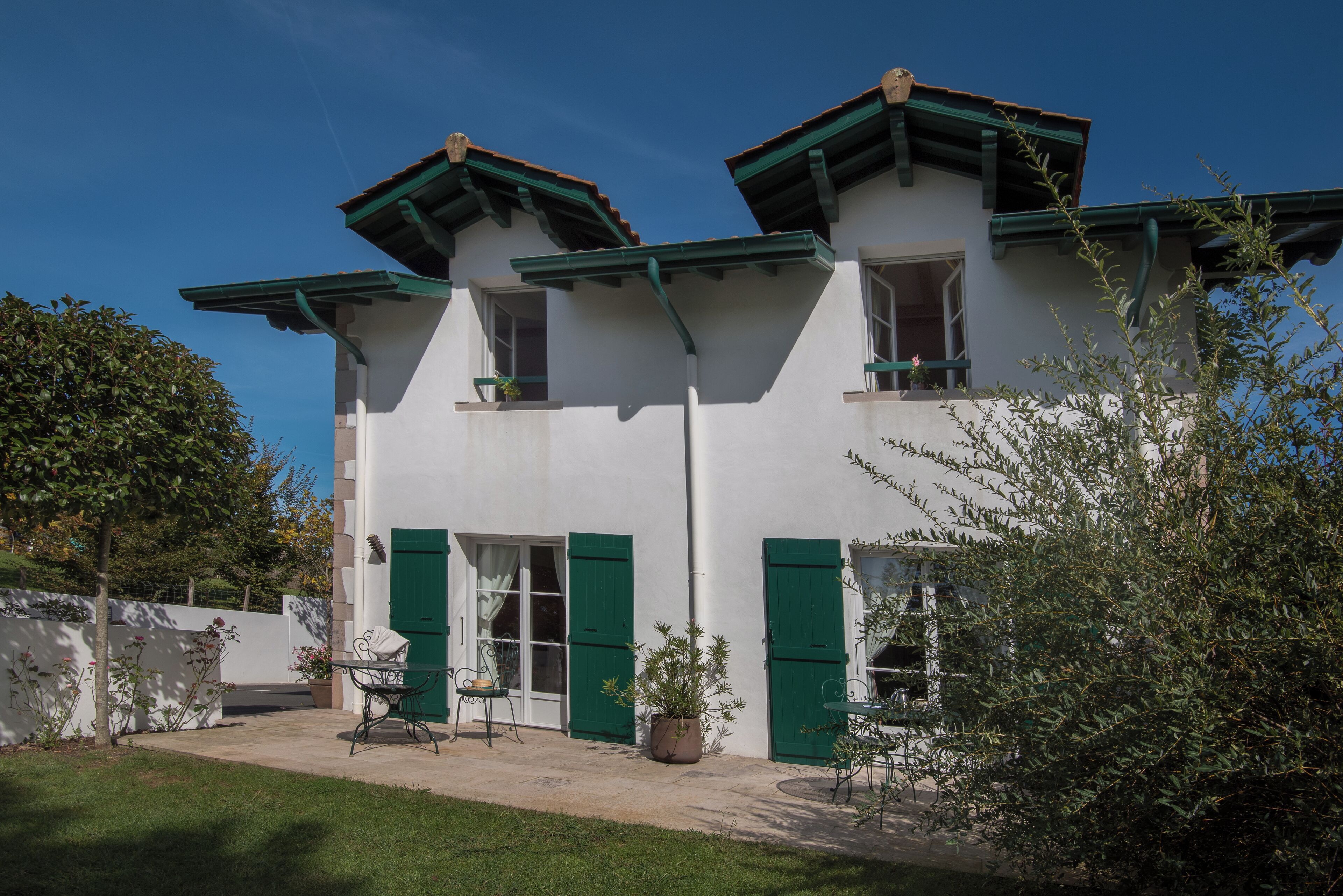 A two-story building with green shutters, a patio with outdoor furniture, and a potted plant.