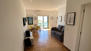 A spacious living area with a wooden parquet floor, a grey sofa, and a dining table with yellow chairs. - Tossan House in Vilamoura Downtown (Quarteira)