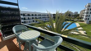 A balcony with wicker chairs and a view of a swimming pool and buildings. - Tossan House in Vilamoura Downtown (Quarteira)