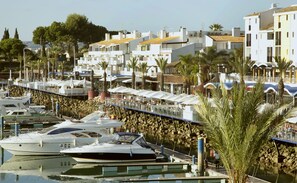Un puerto deportivo con barcos amarrados, un paseo marítimo y edificios al fondo.