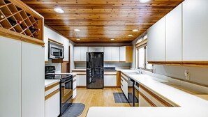 A modern kitchen with wooden ceiling, white cabinets, stainless steel appliances, and a wine rack. - Wildlife Retreat in the Forest (Becket)