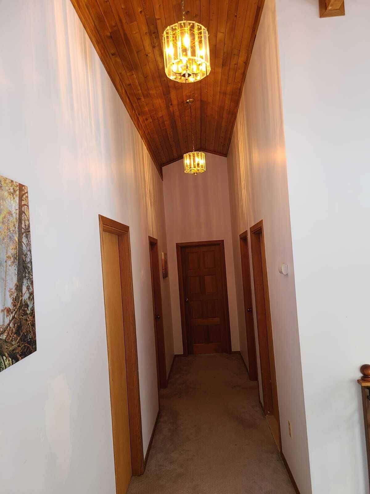 A hallway with wooden ceiling beams, a chandelier, and a door at the end.
