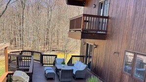 A wooden deck with outdoor furniture, including a table and chairs, and a grill. - Wildlife Retreat in the Forest (Becket)