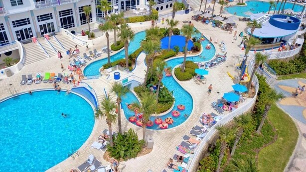 Ein Resort mit mehreren Schwimmbecken, Liegestühlen und Palmen.