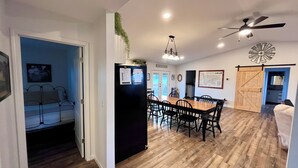 A spacious living area with a dining table, chairs, a black refrigerator, and a ceiling fan.