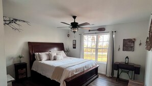 A bedroom with a wooden bed, a ceiling fan, a desk, and a window with curtains.
