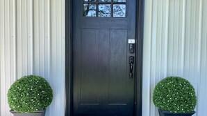 A dark-colored door with a window, flanked by two potted plants, and a wall-mounted light fixture above.