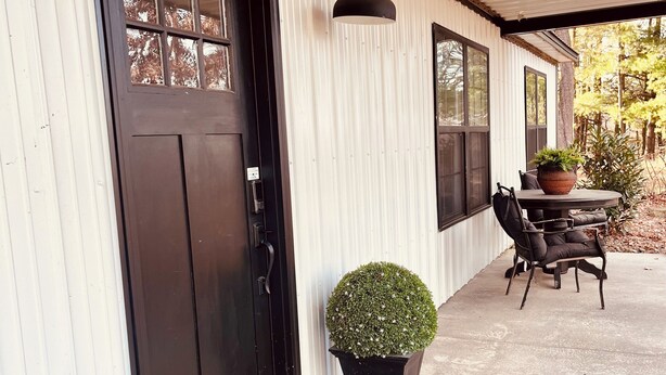 A covered porch with a black door, potted plants, and a table with chairs.
