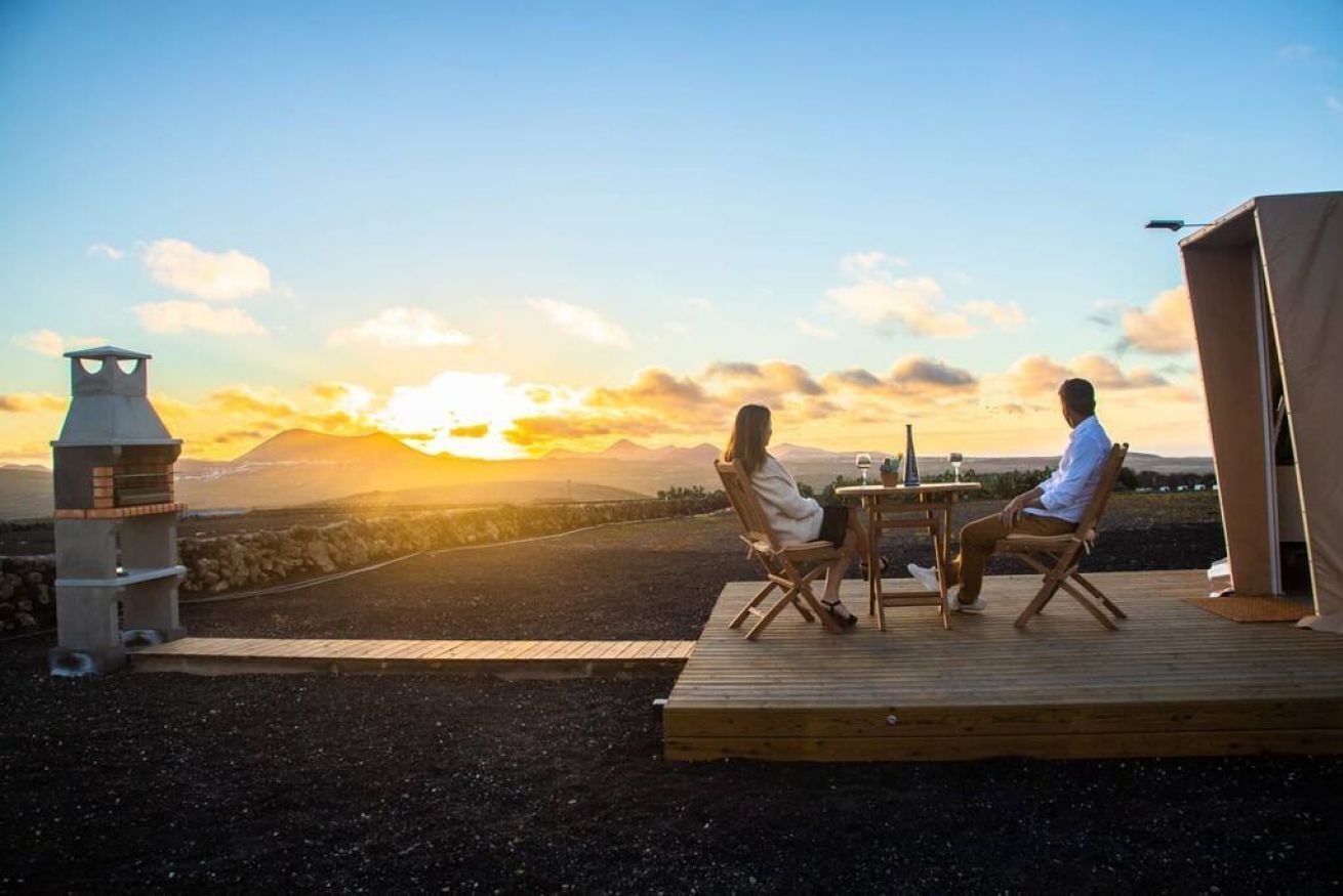 Un couple est assis à une table en bois, face à un paysage montagneux illuminé par le coucher du soleil.