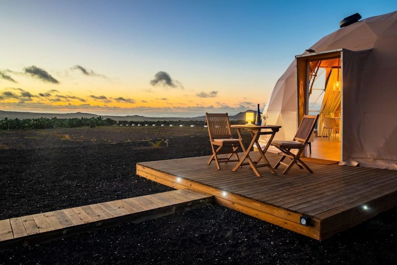 A cozy outdoor seating area with a wooden deck, a table, and two chairs in front of a tent-like structure.