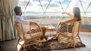 Two people sitting on wicker chairs facing each other with a view of a landscape through a large window.