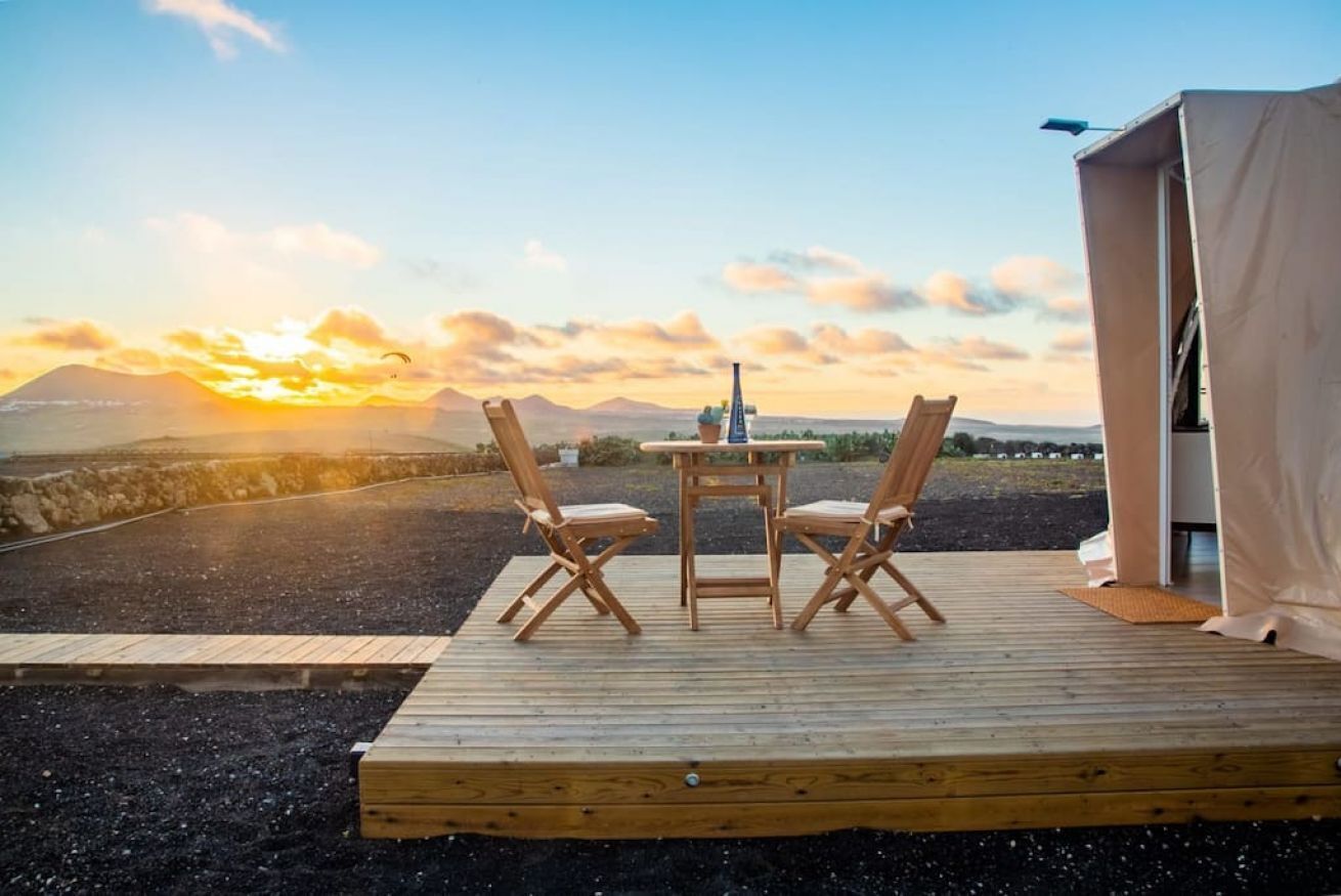 Une terrasse en bois avec deux chaises et une table, offrant une vue panoramique sur un paysage magnifique, avec des montagnes et un coucher de soleil.