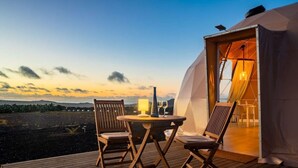 A wooden deck with a table and chairs, a tent with an open door, and a view of the landscape.