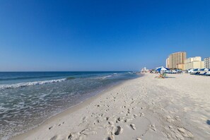 Una platja amb empremtes que condueixen a l'aigua, un cel clar i edificis al fons.