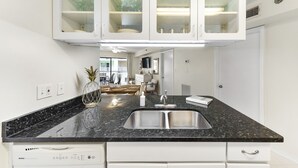 A kitchen with a granite countertop, stainless steel sink, and white cabinetry. - Harbour Place 204 - white sands, and beach view! (Orange Beach)