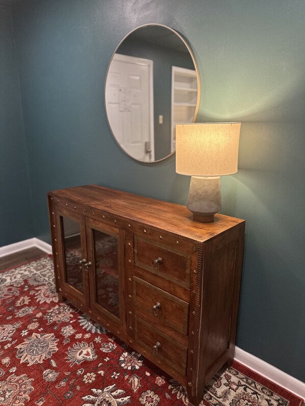 A wooden cabinet with glass doors and a lamp on top, against a teal wall with a mirror above.