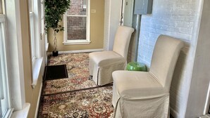 A narrow hallway with a patterned carpet, two beige chairs, a potted plant, and a brick wall with a window. - On Main Street - Apartment C  - Berlin, MD (Berlin)