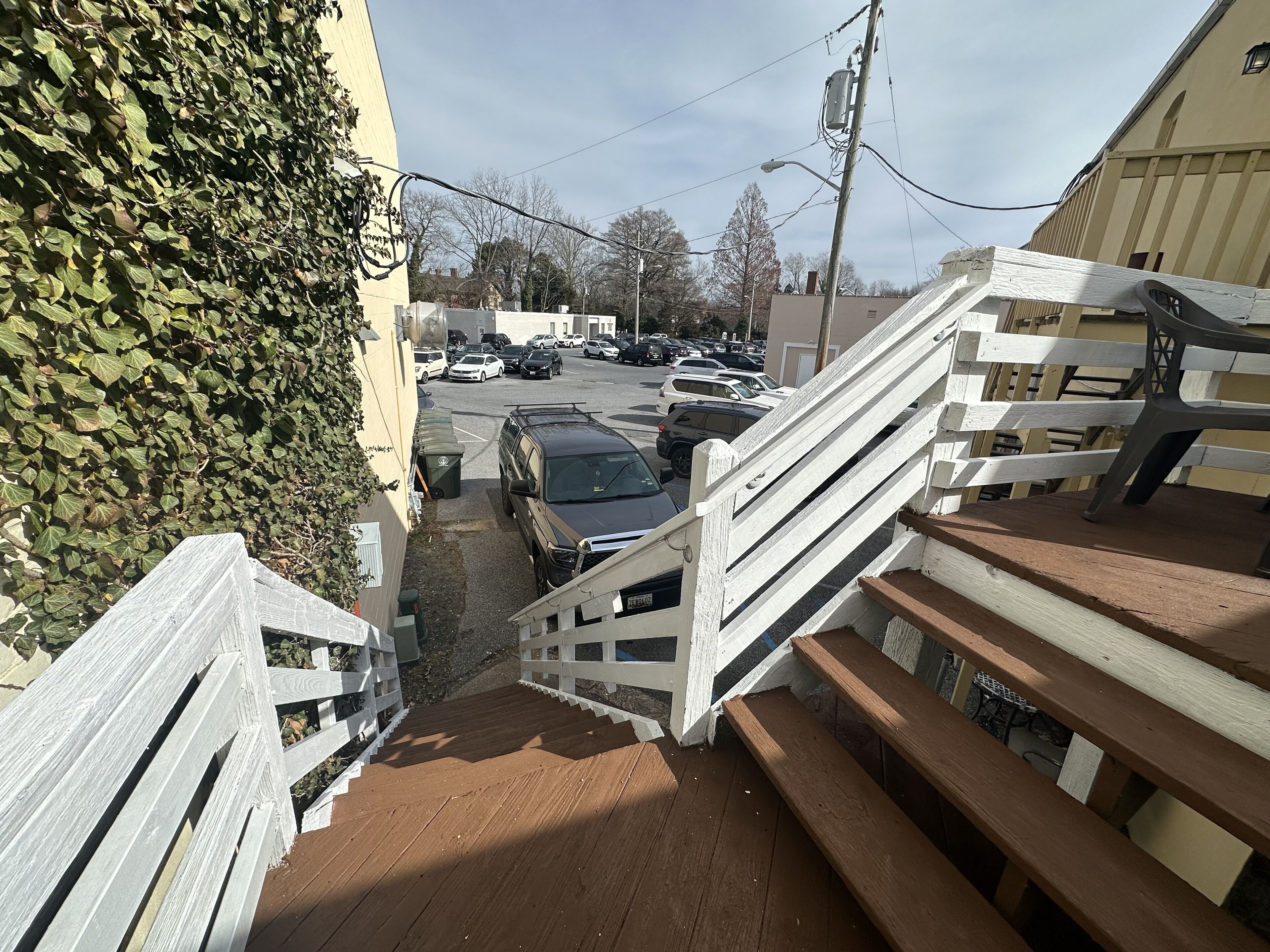 A wooden staircase leading to a parking area with cars and a building in the background.