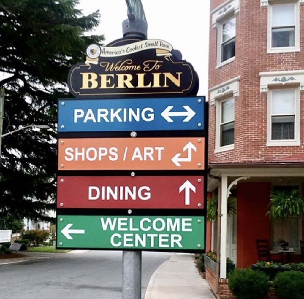 Señal direccional con flechas indicando estacionamiento, tiendas/arte, restaurantes y un centro de bienvenida.