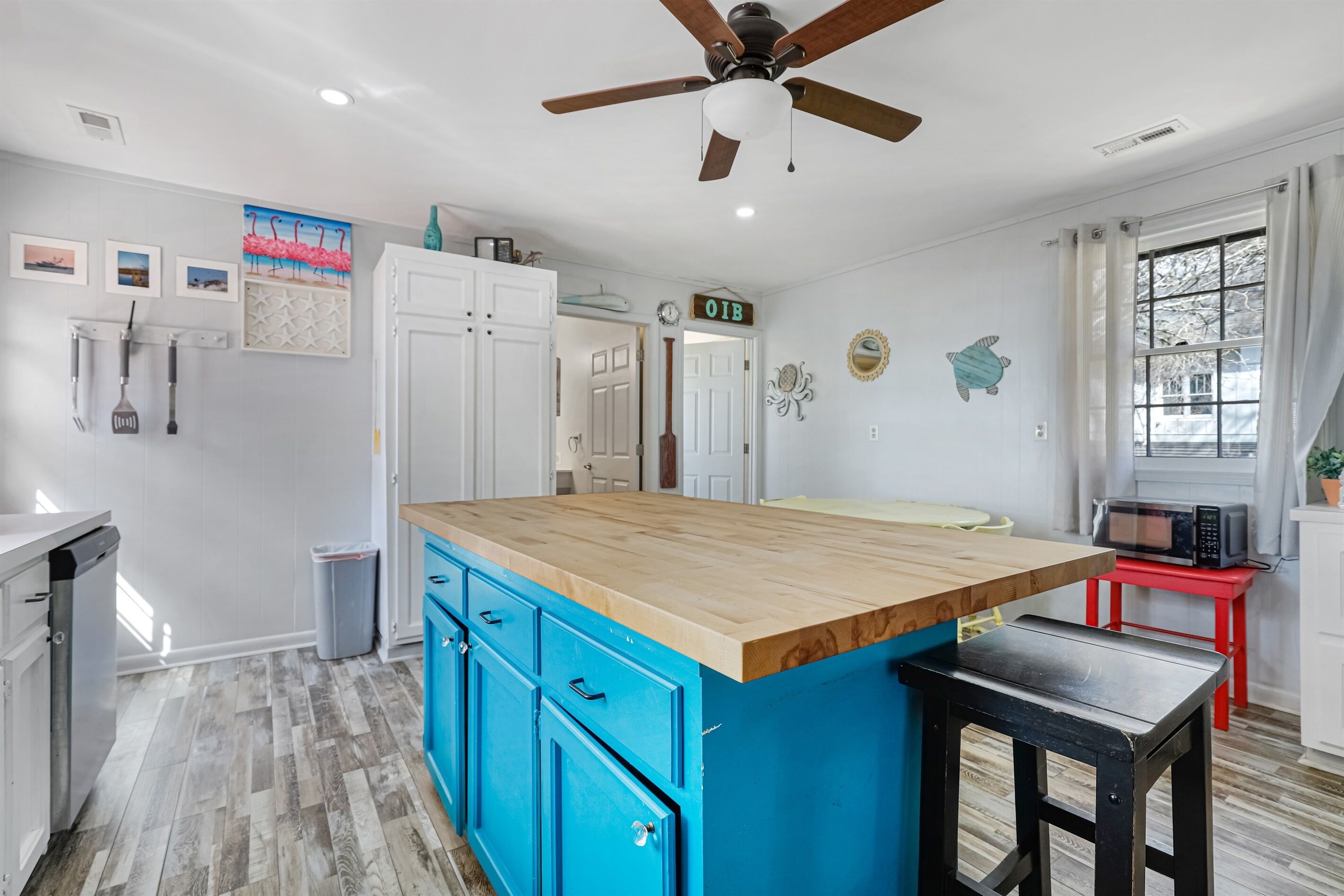 A kitchen with a wooden island, blue cabinets, white appliances, and a ceiling fan.