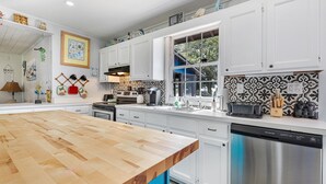 A modern kitchen with white cabinets, a wooden countertop, and a stainless steel dishwasher. - Dolphin Cove • Dazzling Waterfront Cottage w/ Dock (Ocean Isle Beach)