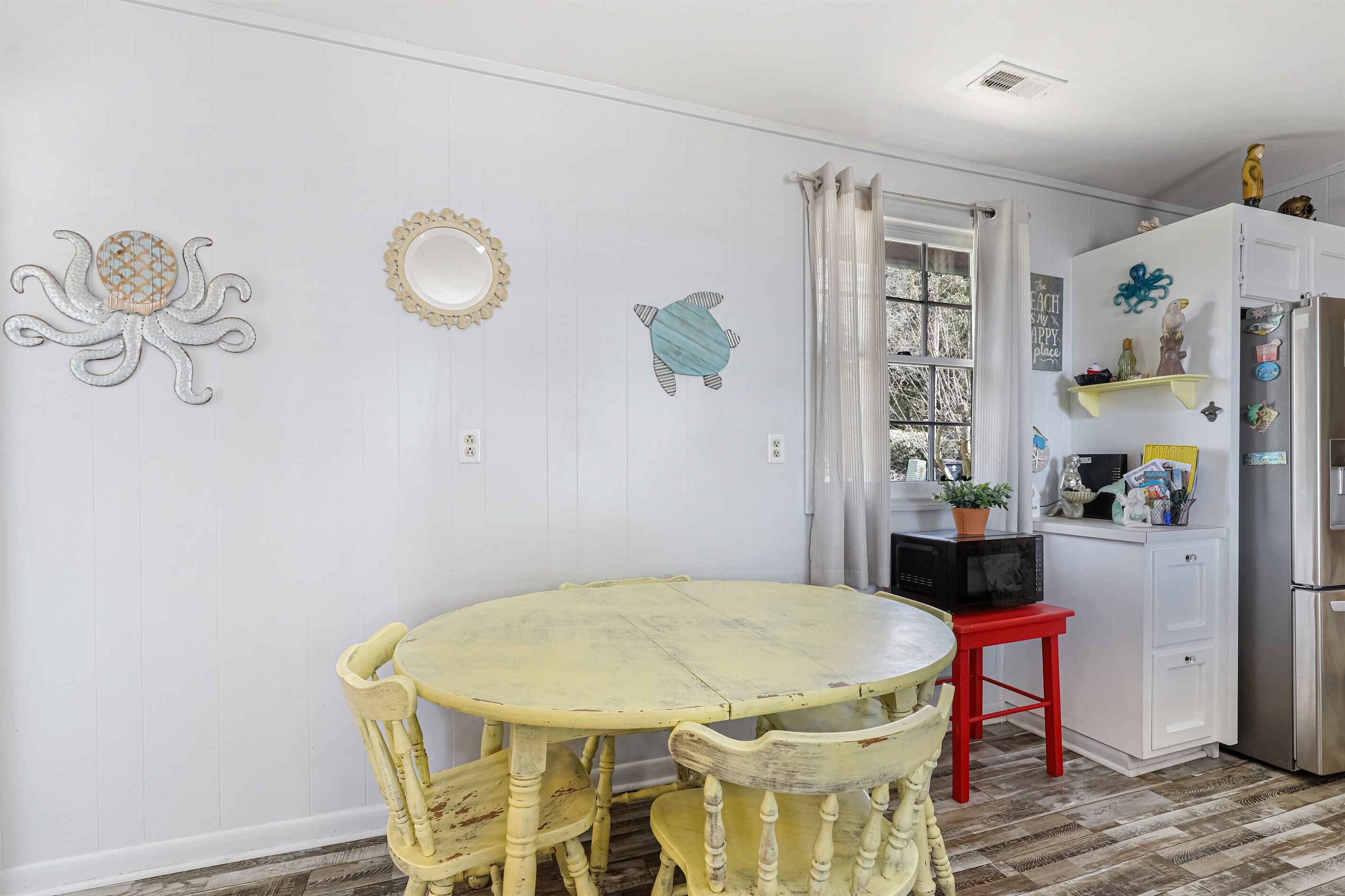 Une cuisine avec une table ronde jaune, des armoires blanches et des œuvres d’art décoratives murales, notamment une représentation d’une pieuvre et d’une tortue.