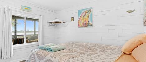 A bedroom with a bed, a window with curtains, a wall-mounted drying rack, and a painting of a whale.