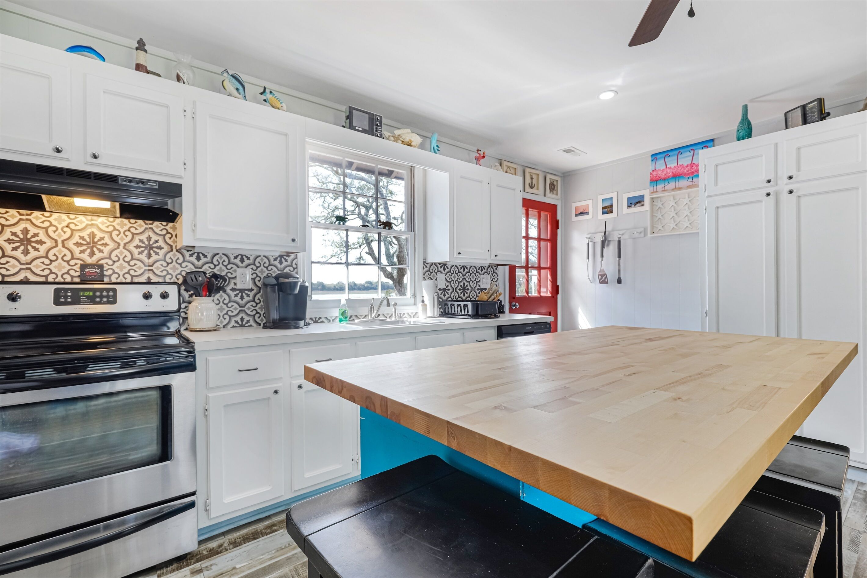 A kitchen with white cabinets, a wooden countertop, and a red door.