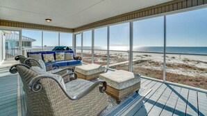 A covered deck with wicker furniture, a blue sofa, and a view of the beach. - Spacious Gulf Front Home on Extra Wide Lot! (Port St. Joe)