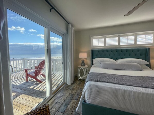 A bedroom with a large window, a bed, a nightstand, and a red chair on a wooden deck. - Spacious Gulf Front Home on Extra Wide Lot! (Port St. Joe)