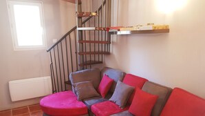 A living room with a brown sofa, red cushions, a red ottoman, a staircase with metal railings, and a shelf with boxes.