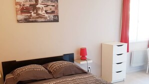 A bedroom with a bed, a nightstand, a lamp, a dresser, and a painting on the wall.
