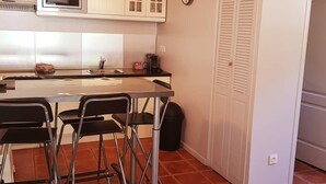 A compact kitchen with white cabinets, a microwave, a sink, and a dining area with chairs.