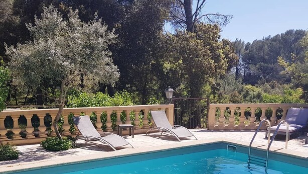 A clear blue pool with lounge chairs and a stone balustrade.