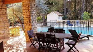 A covered patio with a pool, stone walls, and outdoor furniture.