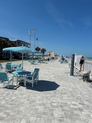 Ein gepflasterter Weg mit Außenbestuhlung, Flaggen und Blick auf den Strand.
