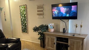 A living room with a television, a leather sofa, a coffee table, a cabinet, and a wall with a plant and a sign. - On the beach (Daytona Beach)