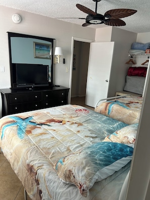 Ein Schlafzimmer mit einem Bett, einem Fernseher auf einer Kommode, einem Deckenventilator und einer Tür zu einem anderen Raum.