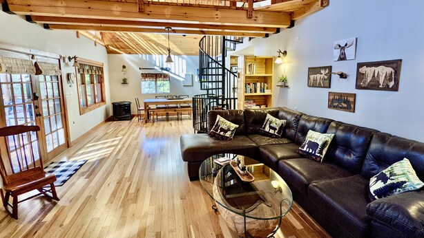 Un amplio salón con suelo de madera, un sofá de cuero, una mesa de centro de vidrio y una escalera que sube a un nivel superior.