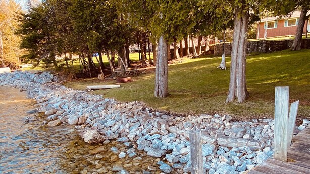 Un arroyo pedregoso con una pasarela de madera y árboles al fondo.