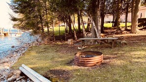 Un camping con un brasero metálico, una mesa de picnic y un tronco.