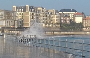 Eine Uferpromenade mit einer Fontäne, einem Geländer und Gebäuden im Hintergrund.