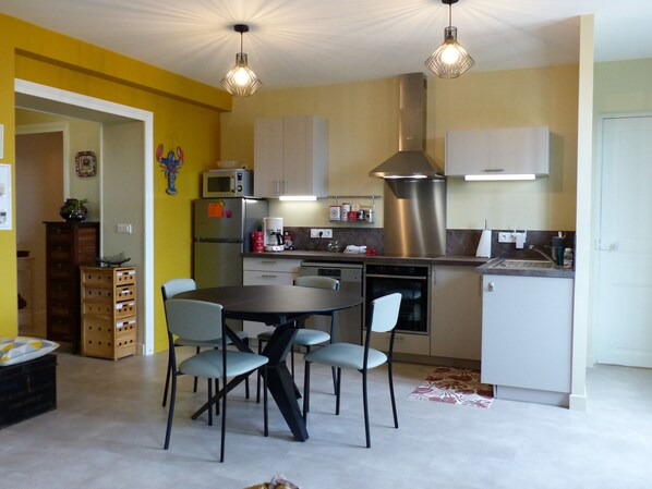 A modern kitchen with a dining area, featuring a round table, four chairs, a microwave, a coffee maker, and stainless steel appliances.