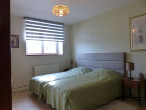 A bedroom with a bed, a bedside table with a lamp, a window with blinds, and a radiator.