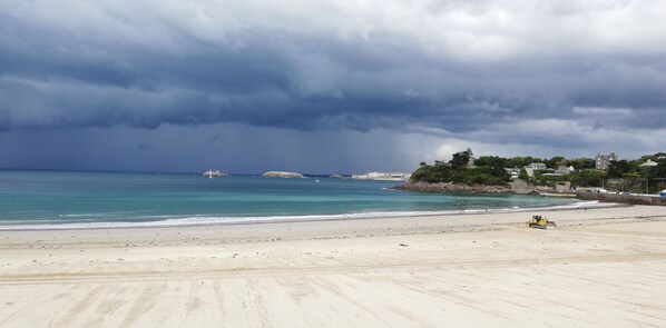 En strand med sandet bredde, et par både i vandet og en overskyet himmel.