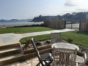 Un patio con vista al mar, escalones de piedra y mobiliario de madera.